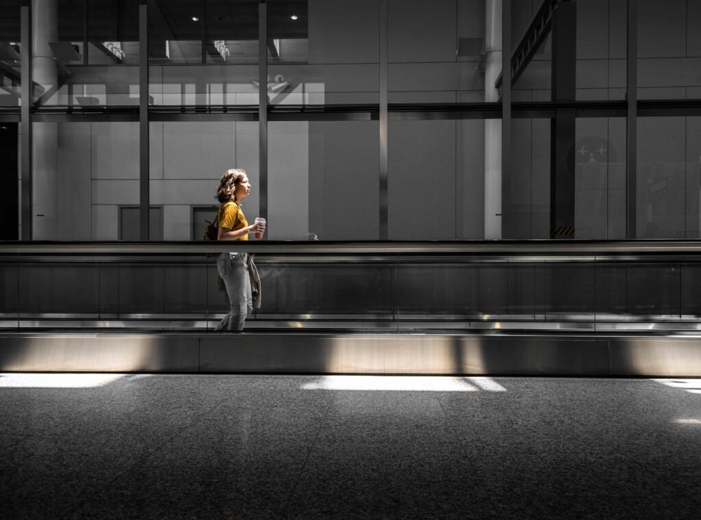 Side view of a woman walking through an airy Toronto airport terminal with a plastic cup in hand.