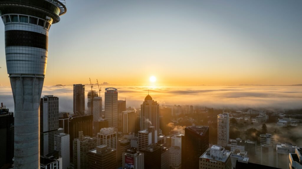 A stunning view of Auckland's skyline with the Sky Tower at sunrise, enveloped in morning fog.
