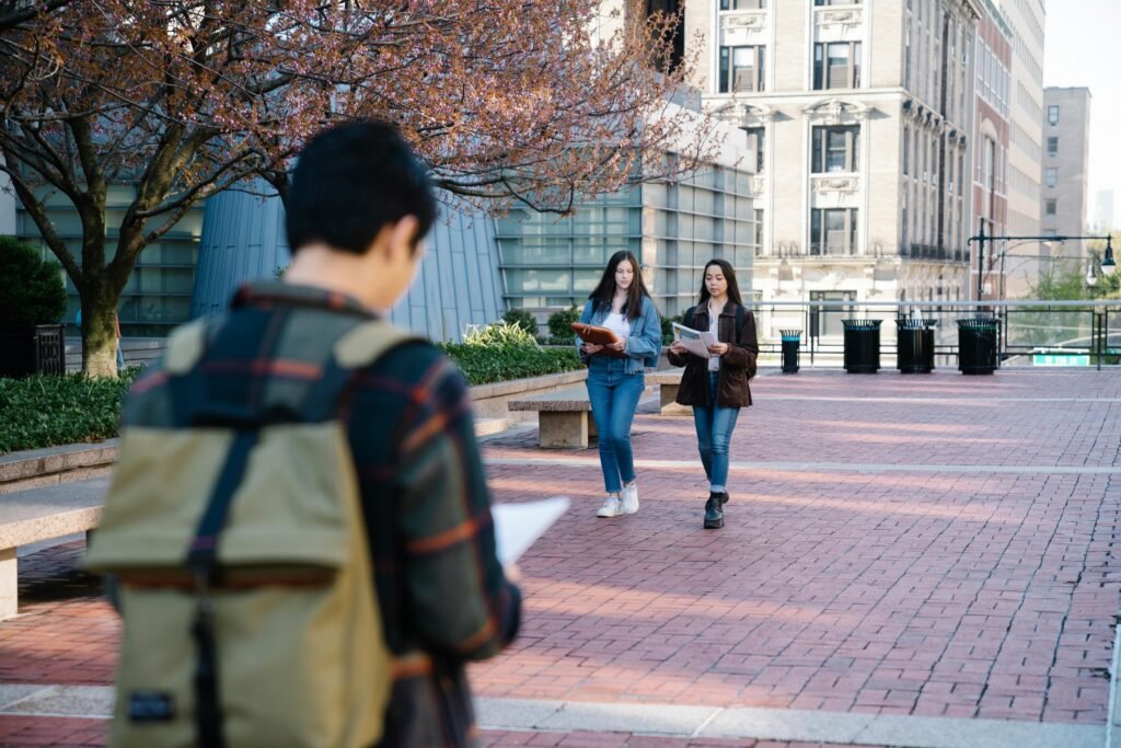 Students stroll through a campus walkway with books and backpacks during daylight.